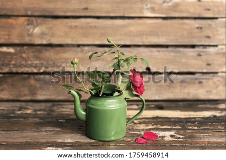 Vintage red roses in old fashion green tea pot on wooden table