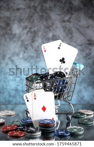 A pair of aces, hearts and diamonds, on a deck of playing cards. Poker playing chips in a blue shopping cart on a light blue background. Online gambling. Addiction. 