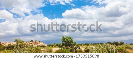 Blue sky and many white big clouds in daylight. Natural sky, mountains and a lot of green trees and grass composition. Ideal for use in the design or wallpaper