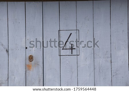 Close front view of part of a grey wooden painted door. Vertical planks with number four written in black. Material pattern with lines.  