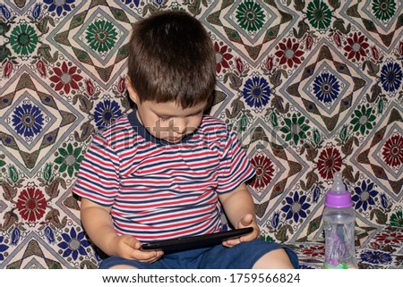 A little boy 2-3 years old looks into the screen of the tablet. Cartoons for children, screen time, children's dependence on the computer and phone.