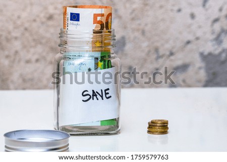 Composition with saving money banknotes in a glass jar with text save. Concept of investing and keeping money, close up isolated.