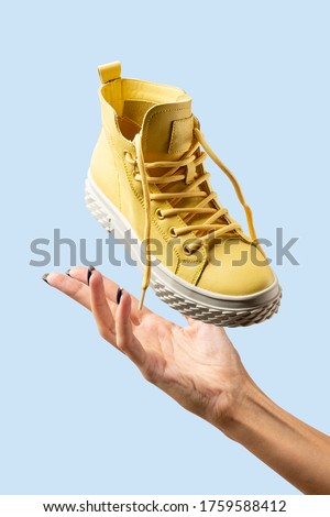 women's hand catches in the air sports yellow sneakers on a blue background, sports shoes on a blue background