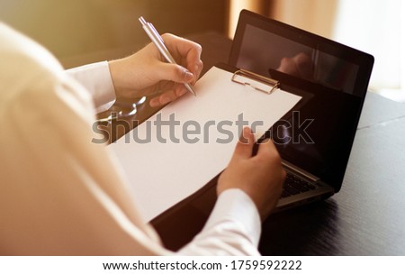male doctor writes on a desk with a laptop on paper