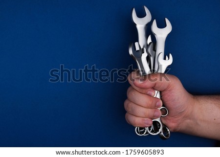 Set chrome spanner keys in mans hand on blue background. Flat lay, top view, minimal composition with copy space.
