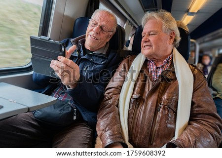 Older man with a good friend in casual wear is taking a self portrait with a smart phone in train in Switzerland at daylight.