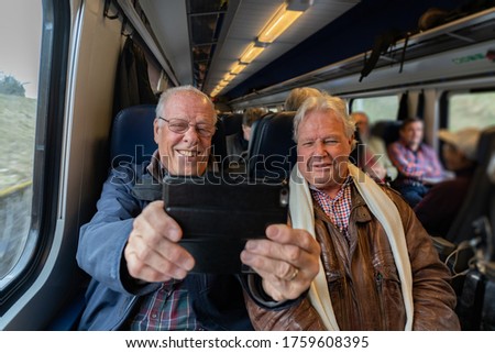 Older man with a good friend in casual wear is taking a self portrait with a smart phone in train in Switzerland at daylight.