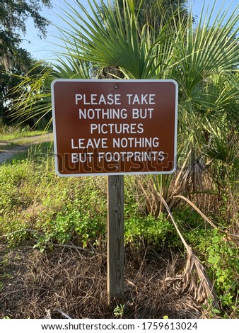 Brown sign in a park that says “Please take nothing but pictures leaves nothing but footprints” that shows that no items should be taken away from the park