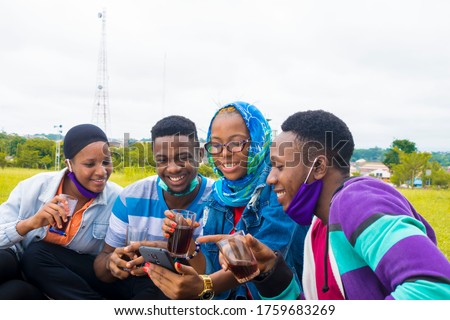 young black people sitting in a park, drinking from their glass cups and using smartphone