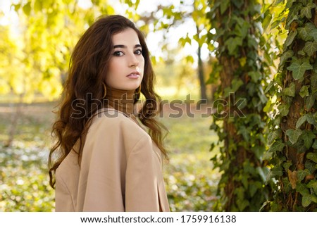 Beauty portrait of a confident girl with curly brunette hair in elegant suit, outdoors, in the park.