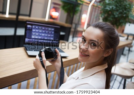 young attractive girl is sitting in front of a laptop and holding camera in her hands. Photographer and Retoucher, study of professional programs for working with photos, online training and practice