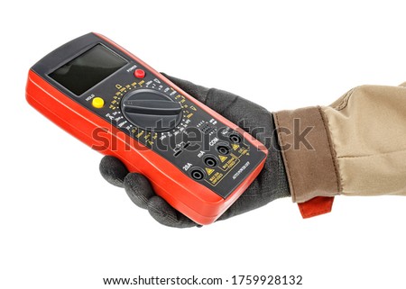 Digital multimeter with red rubber protective case in electrician hand in black protective glove and brown uniform isolated on white background