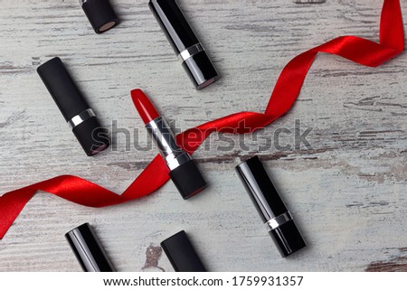 Red lipstick among other lipsticks with red ribbon on light gray background. Fashion, make-up or beauty concept. Copy space. Top view. Flat lay.