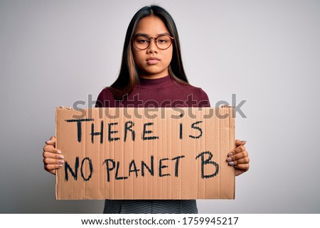 Young asian activist girl asking for environment holding banner with planet message with a confident expression on smart face thinking serious