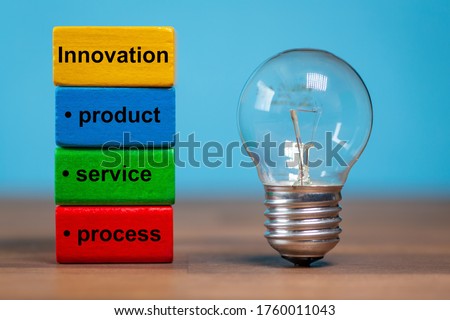 innovation, product, service, process are the words written on colored toy blocks. Next to the tow blocks, an ancient light bulb  stands freely and upright on a dark wooden table.