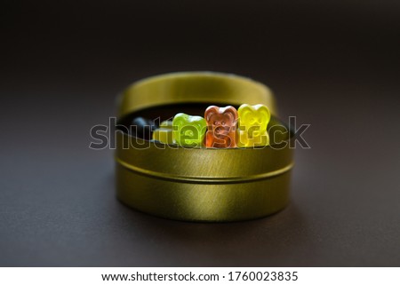 Closeup of three jelly bears peeping out of a round tin candy box on brown background. Selective focus.