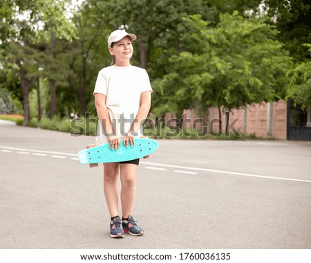 Smiling teenage girl standing on the road and holding penny board in hands. Outdoor portrait of urban sports teenager. Modern summer kids 
activities.