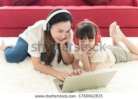 Happiness mother and daughter lie on floor of house use laptop and headphone for entertain , family joyful together in the house