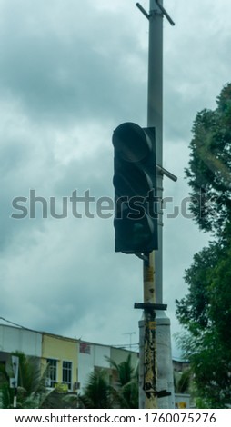 Broken traffic light with no color light up at the side of the road. Selective focus on foreground.