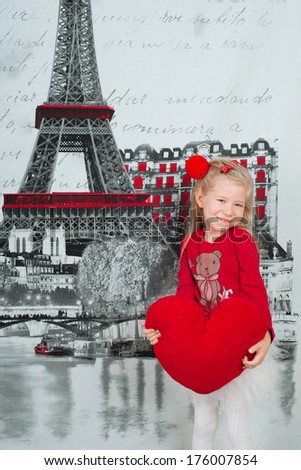 Little girl standing with a heart-shape pillow against image of the Eiffel Tower