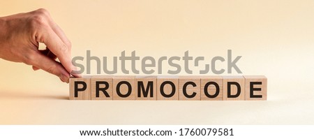 The hand puts a wooden cube with the letter P from the word PROMOCODE. The word is written on wooden cubes standing on the yellow surface of the table. Concept.