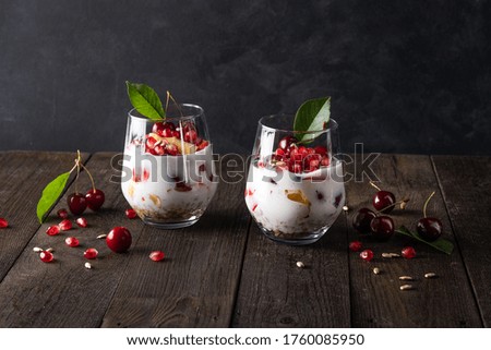 Healthy breakfast in a glass with fresh fruits: pomegranate, cherry, nectarines, honeysuckle, yogurt and granola on a black background. Shallow depth of field with selective focus 