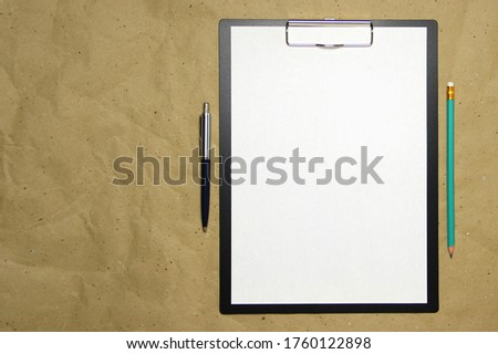 A tablet with a white sheet with pen and pencil on a beige craft paper. Concept of new opportunities, ideas, undertakings, innovations. Stock photo with empty place for your text and design.