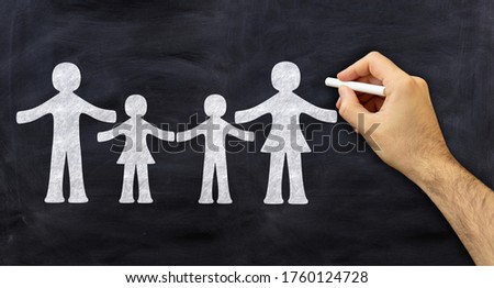 Social issues, family concept. Hand with chalk, sketches a family on blackboard background. Protective parents with the children stand between them.