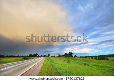 An empty S shape highway (asphalt road) through the green country agricultural field at sunset, Germany. Dramatic clouds after the rain. Idyllic summer rural scene. Dangerous driving, freedom concept