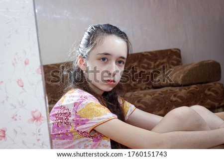 A pretty girl is sitting on the floor in a room near a mirror and looks at her reflection. Close up
