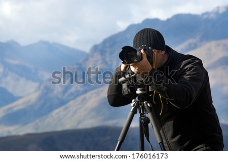 Professional Digital nomad travel photographer and cameraman content creator using camera with telephoto lens on a tripod to photograph and film landscape, nature and wildlife in New Zealand outdoors