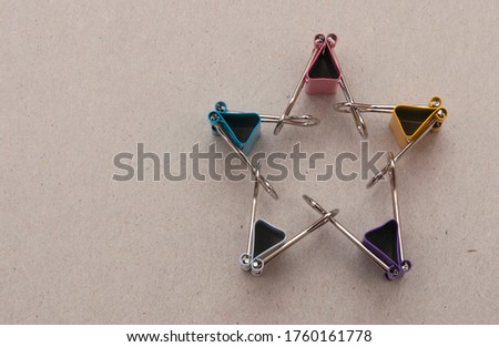 Five binder clips of different colors on a gray paper background represent characters making star figure by holding hands, selective focus
