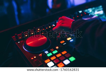 producer  DJ mixer in a nightclub with glowing plays musical rave Dubstep Electronic Trance composition with modern midi controller device in nightclub Live.Musical production process for artists. Royalty-Free Stock Photo #1760162831