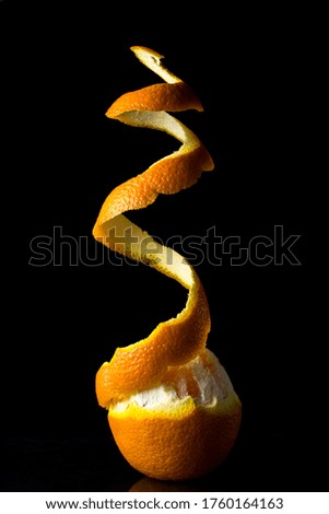 Half peeled orange on a black background. Peel over an orange. Creative photo of an orange. Tropical fruit.