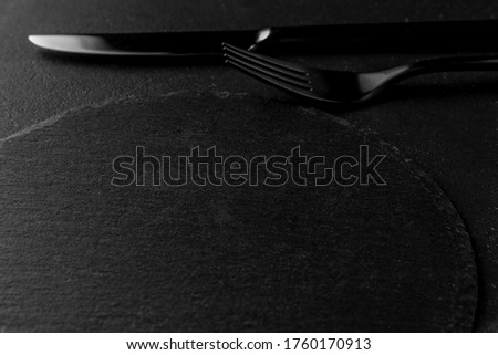 metal fork, knife and round empty black plate from slate stone close-up. dark textured cement background, copy space
