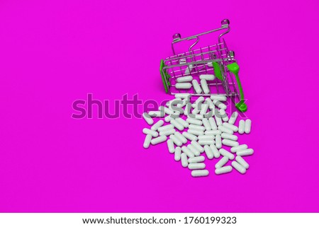 inverted cart with purchased medicines, scattered pills on a violet background, medical concept, vitamins to enhance immunity, protection against diseases, medicines for coronavirus and Covid-19