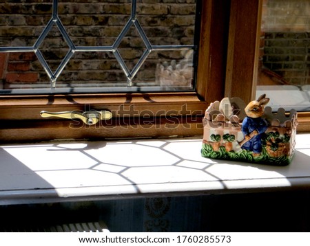 sunlight falls on the window sill through a delicately glazed window, a ceramic figure of a garden-caring hare stands on the windowsill