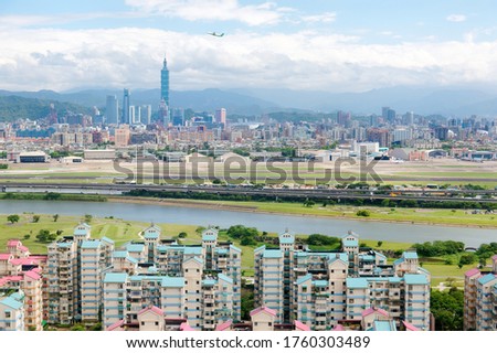 Urban skyline of Taipei, the vibrant capital city of Taiwan, with 101 Tower standing amid skyscrapers in downtown, residential buildings by Keelung River & an airplane taking off from Songshan Airport