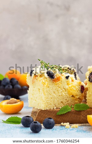 Blueberry and apricot crumble cake decorated with thyme on wooden board. Blue stone background.