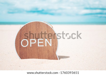 Now open sign board stand on sand summer beach background metaphor to time to travel relax tourism season with copyspace background.