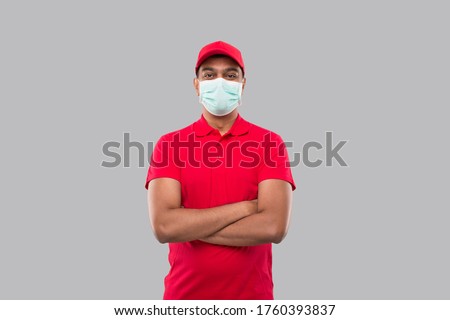 Delivery Man Standing Hands Crossed Wearing Medical Mask Isolated. Indian Delivery Boy in Red Uniform Royalty-Free Stock Photo #1760393837