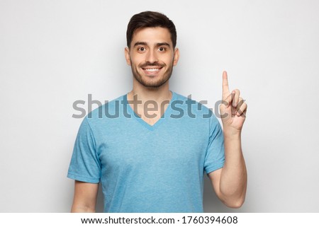 Portrait of excited young man looking at camera, pointing finger up, isolated on gray background
