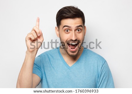 Young excited man in blue t-shirt, pointing upwards with finger, having great idea, isolated on gray background Royalty-Free Stock Photo #1760396933
