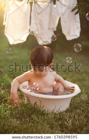 Baby boy bathes in water in a basin in the soap bubbles. Backlit image of sunset.