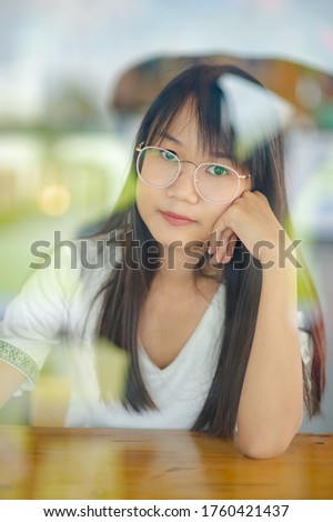 A cute and pretty girl wearing a white T-shirt. She was photographed through clear glass.