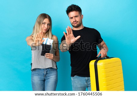 Young caucasian couple going to travel isolated on blue background making stop gesture denying a situation that thinks wrong