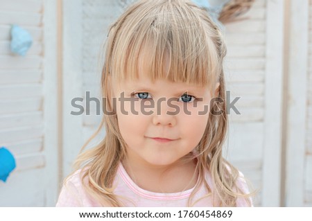 A close-up portrait of a little blonde girl with blue eyes looking at the camera and laughing. Baby plays with shells on the background of marine decoration. Sea adventures and games for children. 