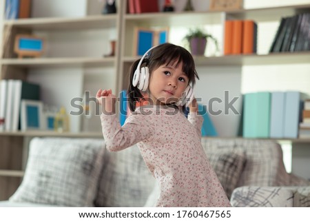 Happy Asian child having fun listening to the music with the headphones and dancing in a room, active leisure and lifestyle concept Royalty-Free Stock Photo #1760467565