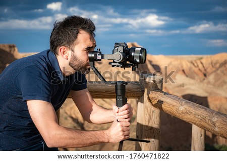 young filmmaker filming natural landscape in canyon with a large river and marshes