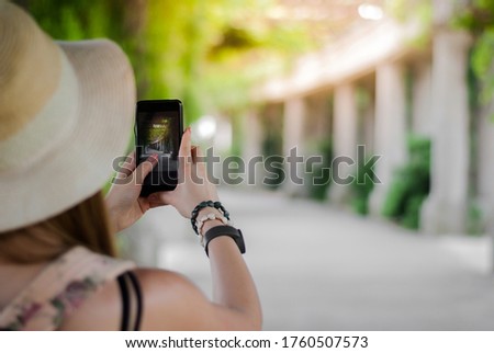 Girl with backpack taking photos of the park road using the smartphone. Close-up shot of the hand holding the phone with the columns arch behind.